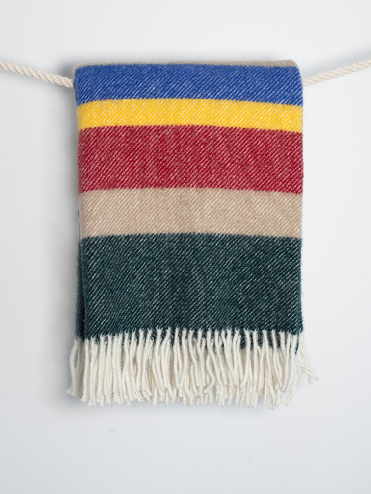Beżowy koc wełniany w wielokolorowe pasy oraz białymi frędzlami